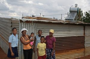 A photo of a family of villagers in Africa in front of a solar panel on top of a roof 