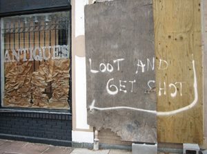 A photo of a damaged building from Hurricane Katrina with a sign posted on the fence that reads, Looters Will Be Shot