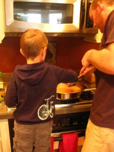 A man and a young boy in the kitchen frosting cookies